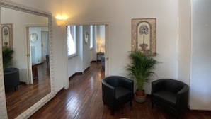 Un hall d’entrée spacieux avec un plancher en bois, un grand miroir, deux fauteuils noirs, une plante en pot et une œuvre d’art encadrée accrochée au mur.