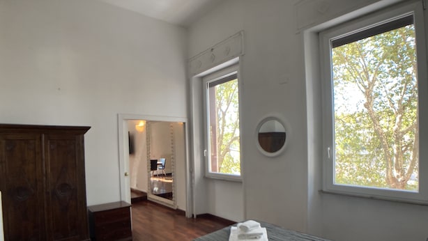 Une chambre à coucher avec un lit, une armoire en bois, un miroir et une fenêtre donnant sur des arbres.