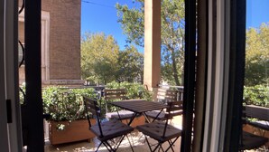 Une terrasse extérieure avec une table et des chaises, entourée de plantes en pot et d’arbres.