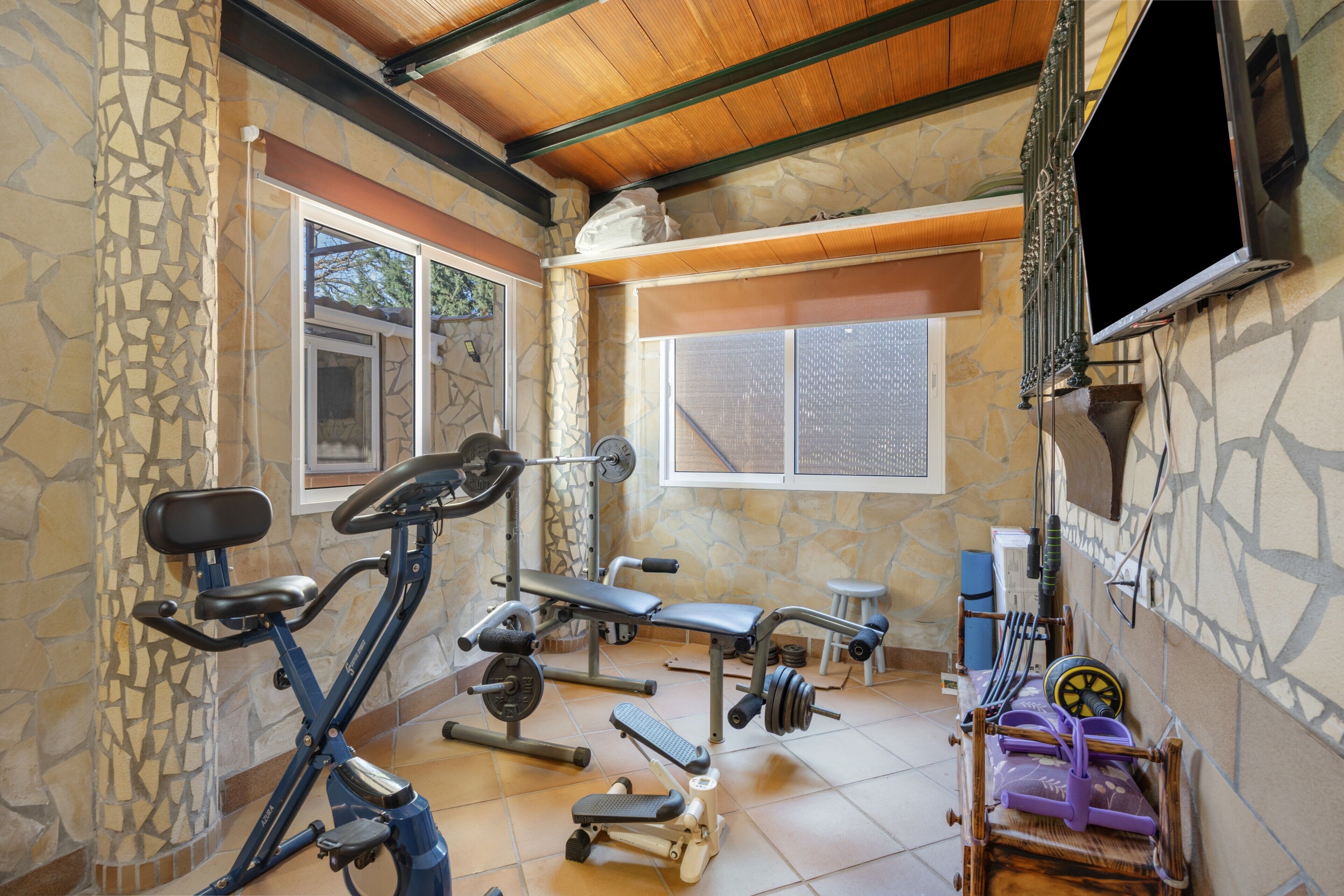 Une salle de sport équipée de matériel d’exercice, d’un banc et d’un téléviseur.