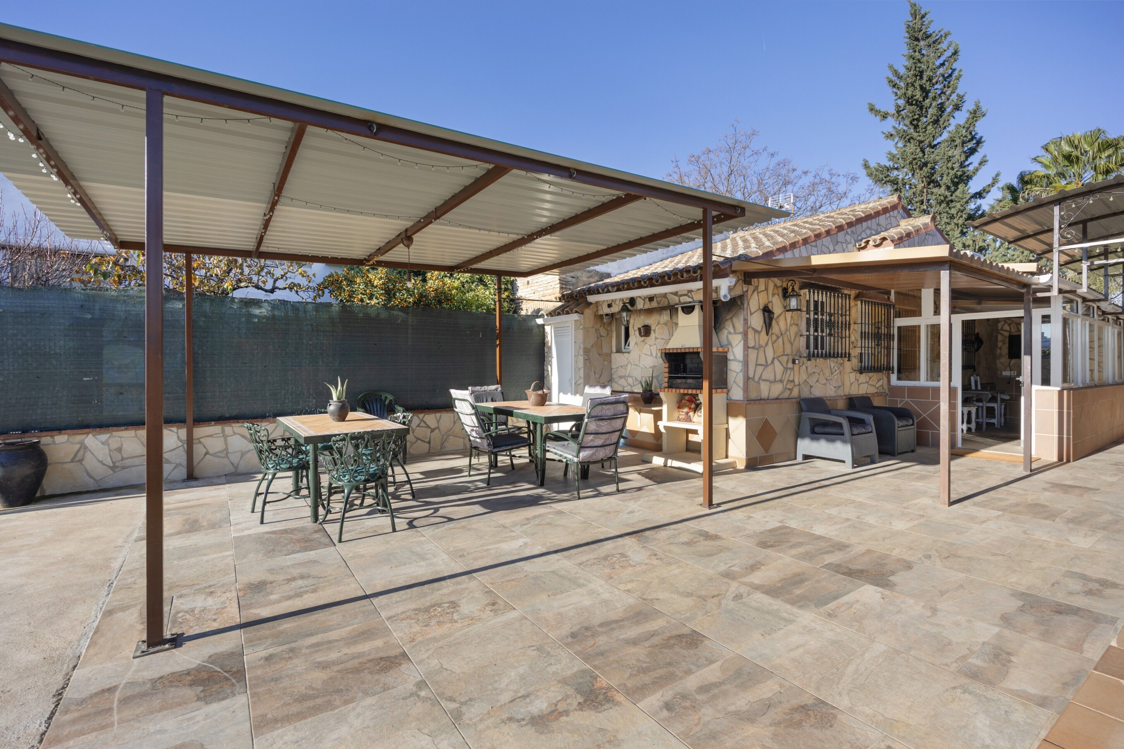 Un'area patio coperta con un tavolo e sedie in pietra, un muro in pietra e vista su una casa con tetto in tegole.