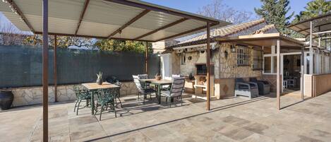 Un'area patio coperta con un tavolo e sedie in pietra, un muro in pietra e vista su una casa con tetto in tegole.