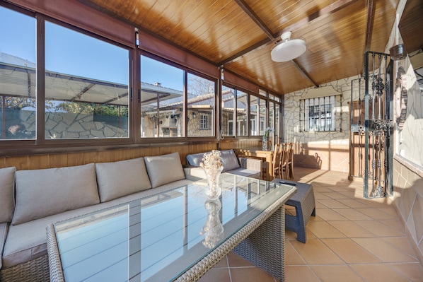 A sunlit room with a glass-top table, cushioned seating, and large windows.