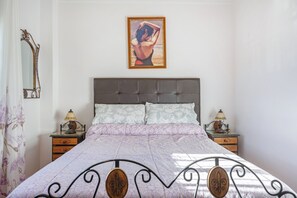 A bedroom with a bed, two bedside tables, a nightstand, a mirror, and a painting on the wall.