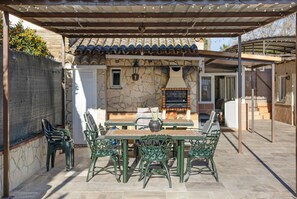 An outdoor patio with a stone wall, a grill, and a table with chairs.