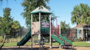Un parque infantil con un tobogán, estructura para escalar y un pequeño refugio.