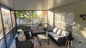 A sunlit patio with wicker furniture, a small table, and a black side table. - The Oaks Bay (Kissimmee)