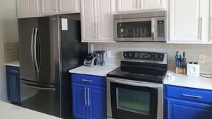 A kitchen with white cabinets, a black refrigerator, a microwave, a stove, and a blue cabinet. - The Oaks Bay (Kissimmee)