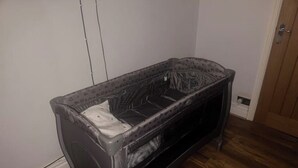 Quarto pequeno, com cama de casal, piso de madeira, paredes brancas e porta de madeira.