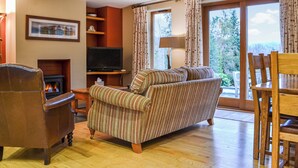 A cozy living room with a fireplace, a television, a striped sofa, and a dining area with wooden chairs. - 3 bedroom accommodation in Keswick (Keswick)