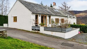 A white house with a sloped roof, a chimney, and a small porch with potted plants. - 3 bedroom accommodation in Keswick (Keswick)