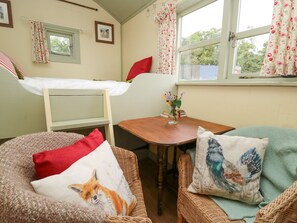 A cozy room with a bunk bed, a small table with a vase of flowers, and two wicker chairs with decorative pillows. - Sweet Briar Shepherds Hut (Brecon)