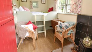 Um quarto acolhedor com uma cama beliche, cadeiras de vime, uma mesinha e uma janela com cortinas florais.