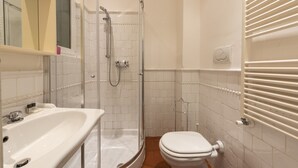 Casa de banho com cabine de duche em vidro, lavatório branco e sanita.