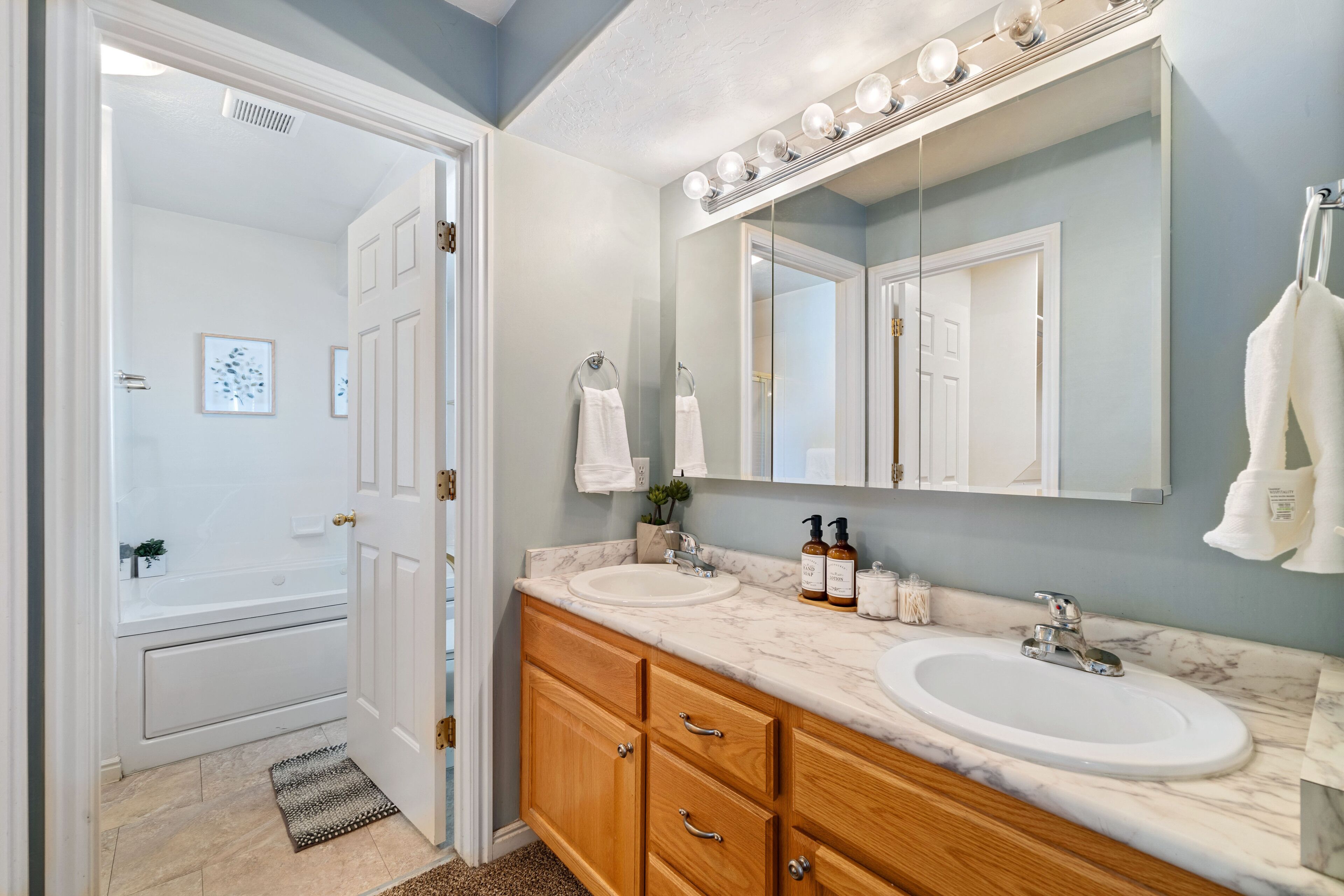 A bathroom with two sinks, a large mirror, and a vanity with wooden cabinets.