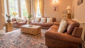 Ein Wohnzimmer mit einem gemusterten Teppich, Ledersofas, einem Holztisch und einem großen Fenster mit Vorhängen.