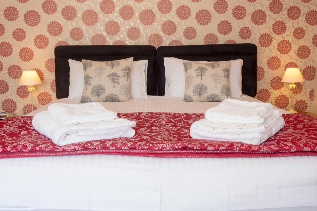 A double bed with a red and white patterned bedspread, two pillows with tree designs, and two lamps on either side.