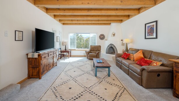 A living room with a wooden ceiling, a television, a fireplace, a sofa, and a patterned rug. - Private and spacious home near the Plaza with mountain views! (Santa Fe)