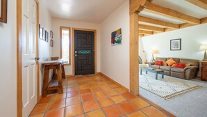 A hallway with a tiled floor, a wooden bench, a door with a decorative handle, and a living area with a sofa and a lamp. - Private and spacious home near the Plaza with mountain views! (Santa Fe)