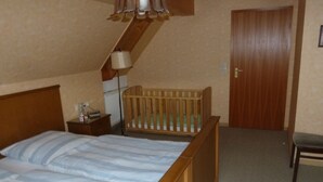 Un dormitorio con una cama de madera, una cuna, una mesita de noche, una lámpara y una puerta.