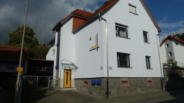 Un edificio de dos pisos con fachada blanca, techo de tejas rojas y puerta amarilla.