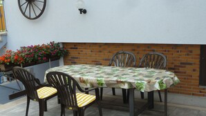 Un patio al aire libre con una mesa y cuatro sillas, un muro de ladrillo, una jardinera con flores y un aplique de pared.