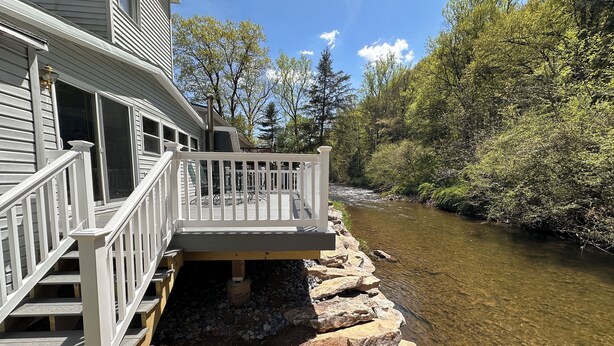 Une terrasse en bois, dotée d’une rambarde, mène à une maison avec une porte de garage. Une rivière longe la terrasse.