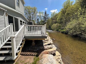 A wooden deck with a railing leading to a house with a garage door. A river runs alongside the deck.