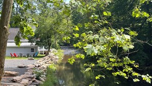 Une vue sur la rivière, avec un mur de pierres, une rangée de fauteuils Adirondack et un chalet en arrière-plan.