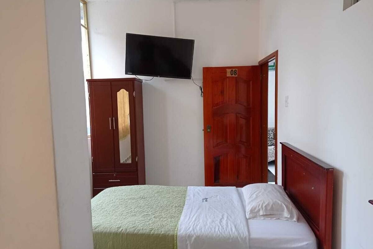 A bedroom with a bed, a television mounted on the wall, a wardrobe, and a door.