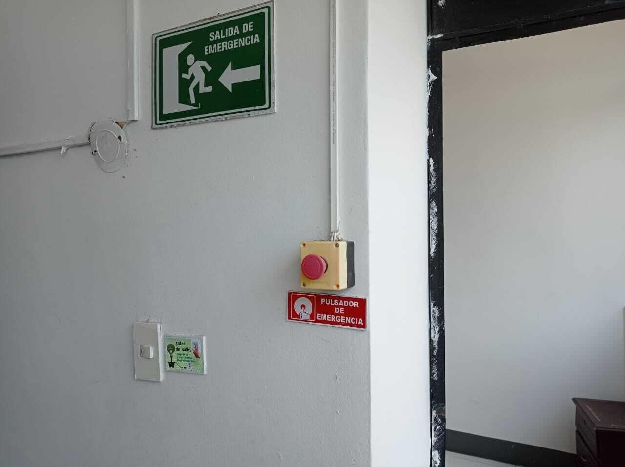 An emergency exit sign, a fire alarm button, and a smoke detector on a wall.