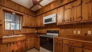 A kitchen with wooden cabinets, a white microwave, and a stove. - Authentic Ranch Home on 650 Acres with Peace and Tranquility (Marble Falls)