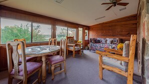 A wooden interior with a round glass table, wooden chairs, a sofa, and large windows offering a view of trees. - Authentic Ranch Home on 650 Acres with Peace and Tranquility (Marble Falls)