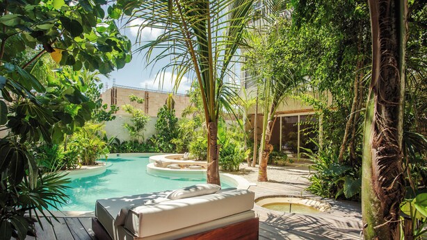 Una terraza de madera con una cama empotrada y una piscina rodeada de abundante vegetación.