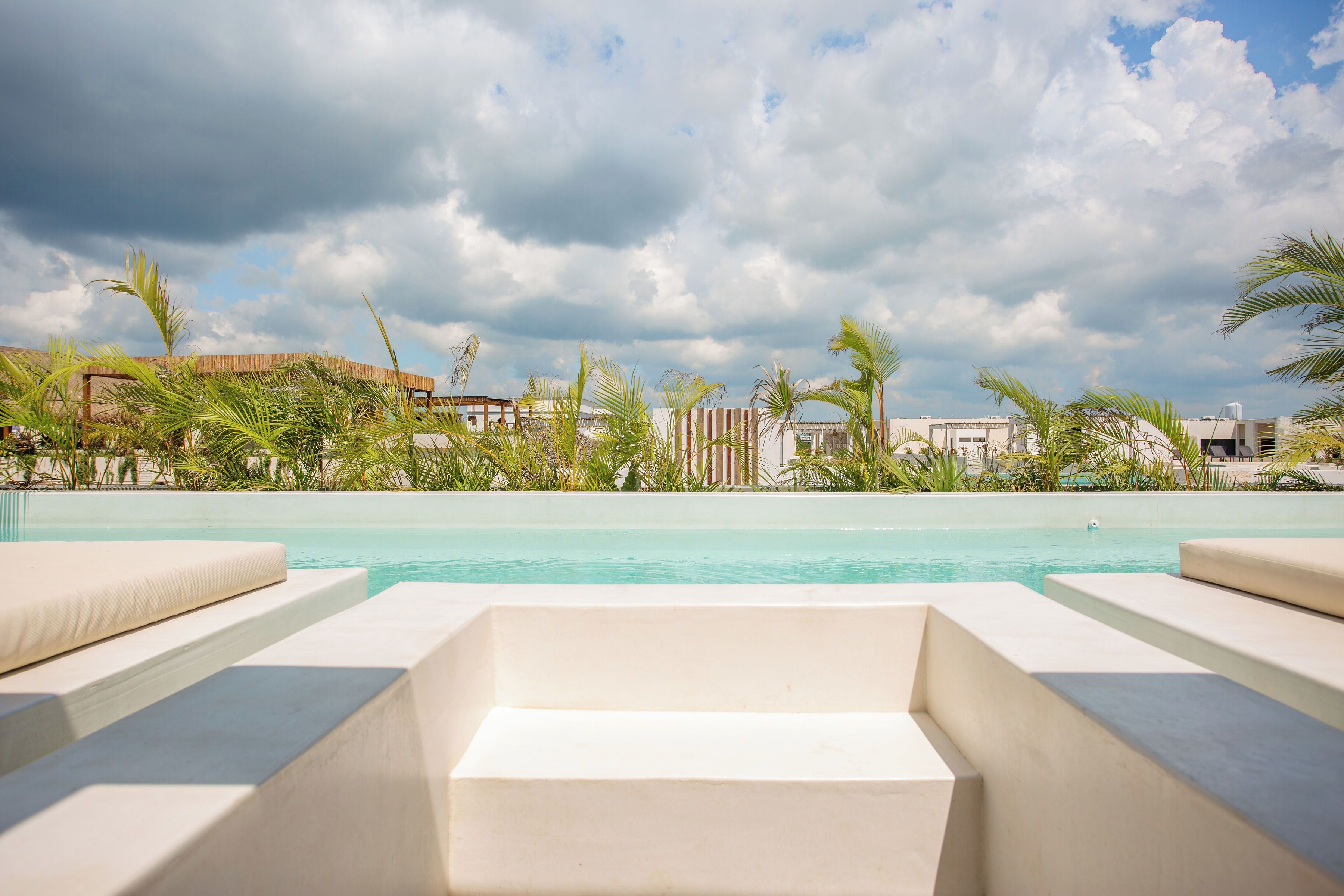 A pool area with white lounge chairs, palm trees, and a building in the background.