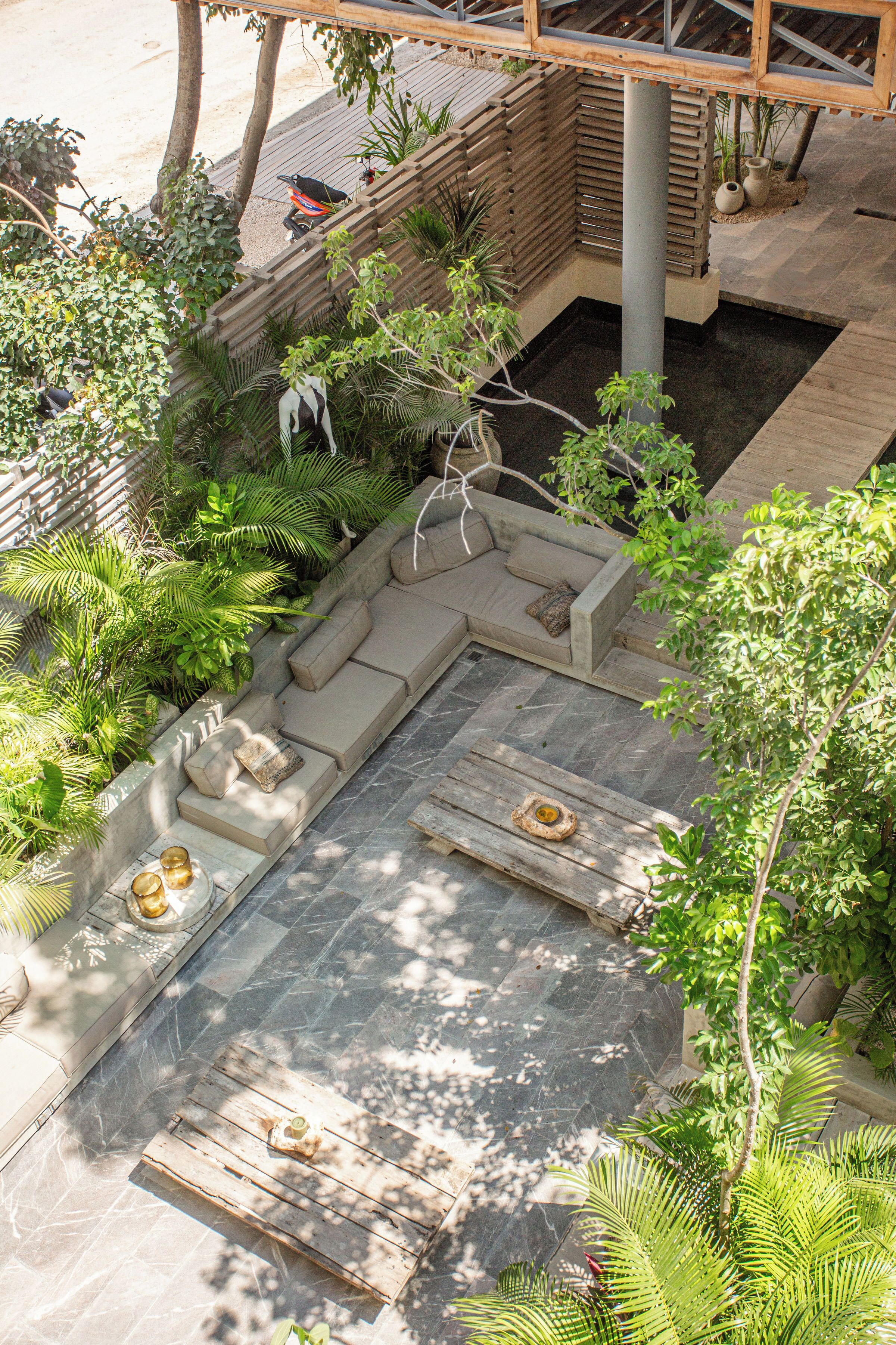 A rooftop garden with a wooden deck, a stone fire pit, and a seating area with cushions.