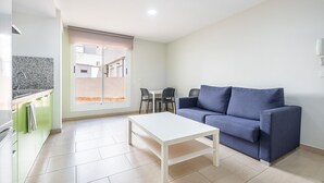 Un salon moderne avec une table basse blanche, un canapé bleu et un coin cuisine doté d’un plan de travail en granit.