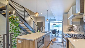 A modern kitchen with a central island, stainless steel appliances, and a staircase with a plant. - City Skyline Views: Upscale Denver Townhome (Denver)