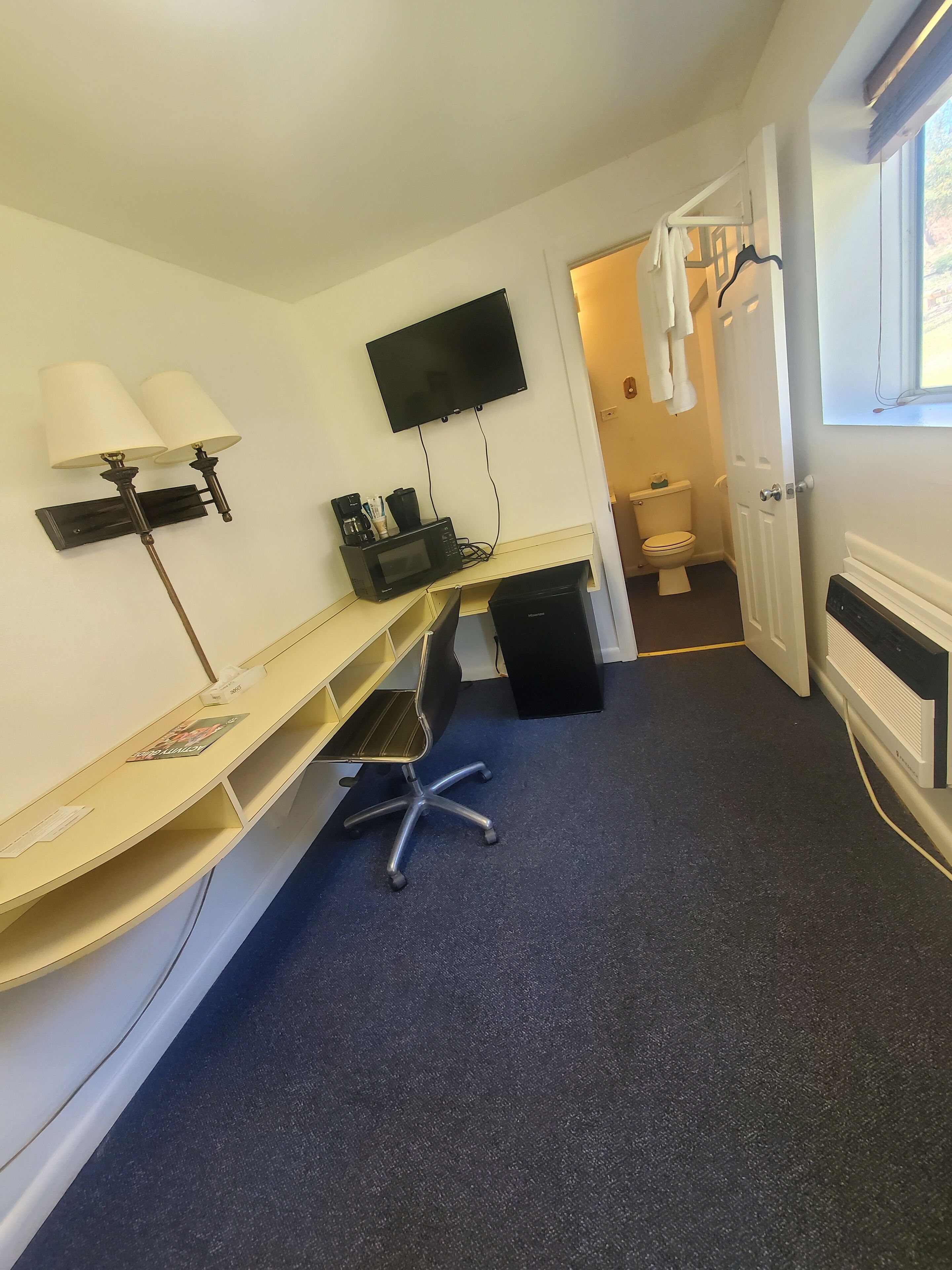 Une chambre d’hôtel compacte équipée d’un bureau, d’une télévision à écran plat, d’un four à micro-ondes et d’une machine à café.