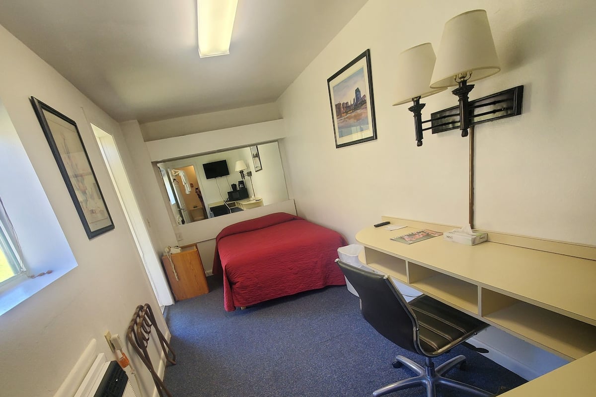 A hotel room with a bed, desk, chair, and a large mirror.