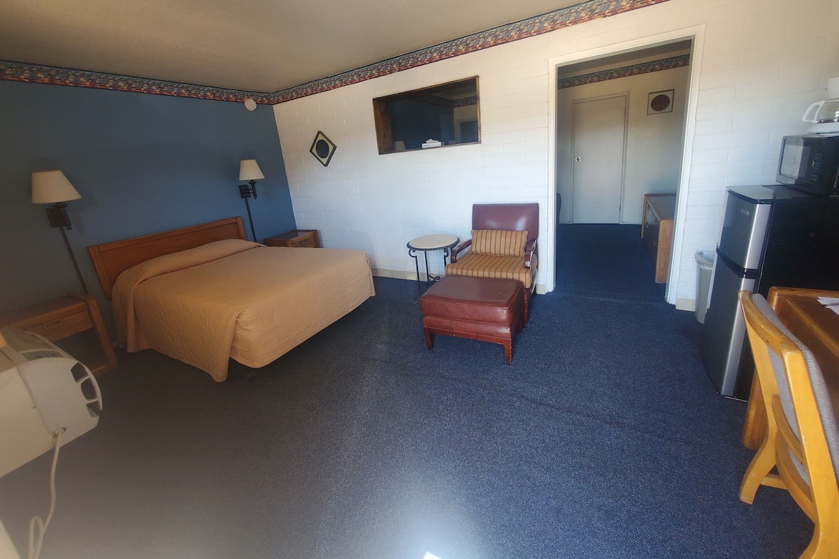 A hotel room with a bed, a chair, a small table, a microwave, and a refrigerator.