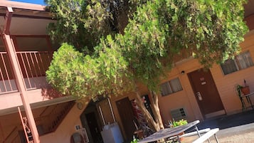 A building with a covered outdoor area, a staircase, and a tree providing shade.