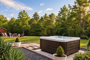 Un bain à remous dans un jardin, avec une terrasse en bois, des plantes en pot et du mobilier d’extérieur.