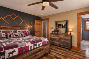 Un dormitorio con una cama de madera, un aparador, un ventilador de techo y una puerta.