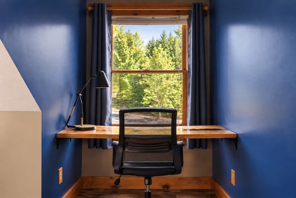 Una habitación con escritorio, silla y ventana con cortinas.