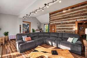 Un salon moderne avec un canapé d’angle, un plancher en bois, une table basse en bois et un mur en bois brut.