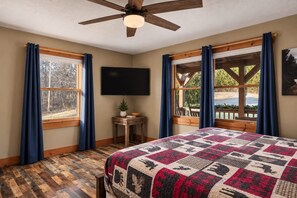 A bedroom with a large bed, a ceiling fan, a flat-screen TV, and a window with curtains.