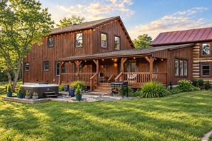 A rustic log cabin with a covered porch, outdoor seating, and a hot tub.