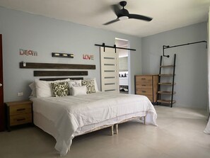 Ein Schlafzimmer mit einem Bett, einem Nachttisch, einer Kommode, einem Deckenventilator und einem Kleiderschrank mit Spiegel.