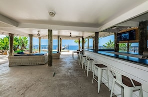 Un espacio al aire libre techado con un bar, asientos y vistas al mar.